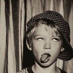 a young boy sticking his tongue out with a hat on top of his head in front of a curtain