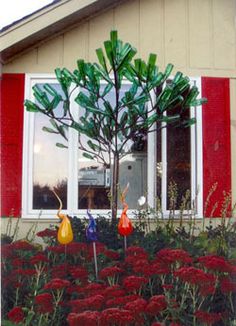 a house with red and yellow flowers in the front yard, and a tree that has been made out of plastic bottles