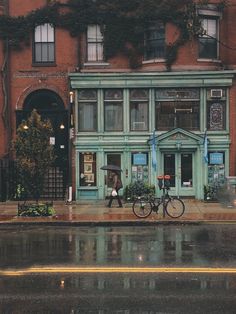 two people walking down the street in front of an old building on a rainy day