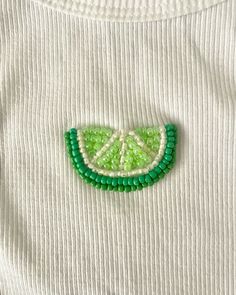 a white t - shirt with green beads and a piece of fruit on it's chest