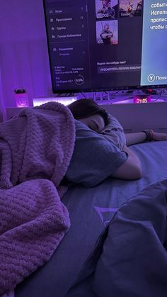 a person laying on a bed with a blanket over their head in front of a flat screen tv