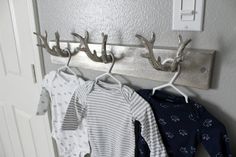 three baby clothes hanging on a coat rack in a room with a white door and light switch