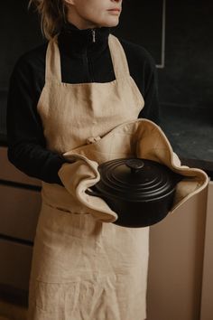 a woman in an apron holding a black pot