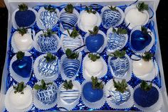 a box filled with blue and white chocolate covered strawberries on top of each other