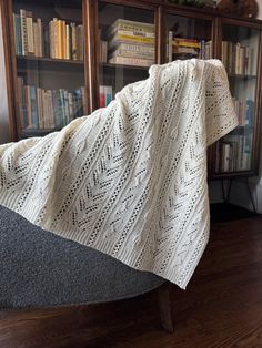 a blanket is draped over a chair in front of a bookcase with books on it