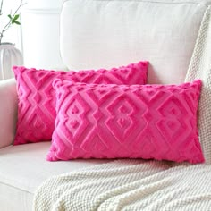 two pink pillows sitting on top of a white couch