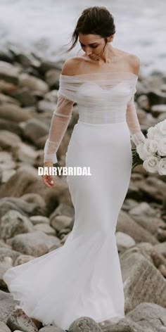 a woman in a white wedding dress walking on rocks near the ocean with her bouquet