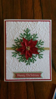 a christmas card with poinsettis and ribbon on the front, sitting on a wooden table