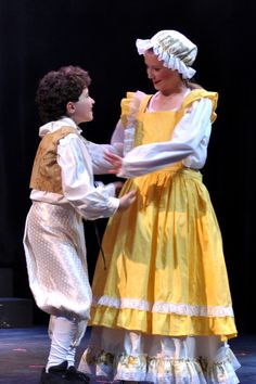 two people dressed in period clothing on stage with one holding the other's hand