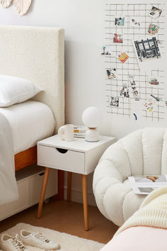 a bedroom with a bed, nightstand and white chair in front of a wall with pictures on it