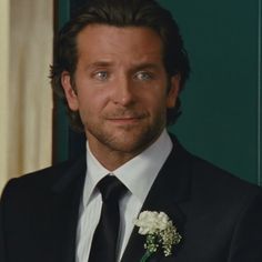 a close up of a person wearing a suit and tie with a flower in his lapel