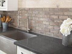 a kitchen with black counter tops and white cupboards next to a brick backsplash