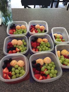 six plastic containers filled with fruit on top of a counter next to a vase full of flowers