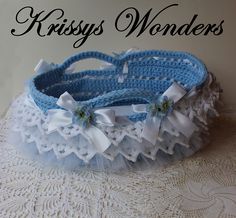 a blue and white crocheted basket with bows on it sitting on a lace doily