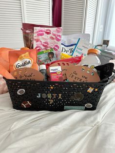 a black basket filled with lots of items on top of a white bed next to a window