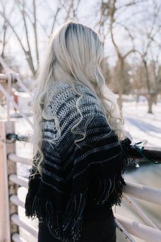 a woman with long blonde hair wearing a black and white knitted sweater looking over a fence