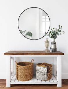 a white console table with two baskets and a round mirror on the wall above it