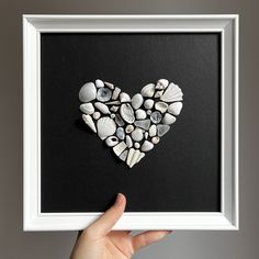 a hand holding up a framed photo with shells in the shape of a heart