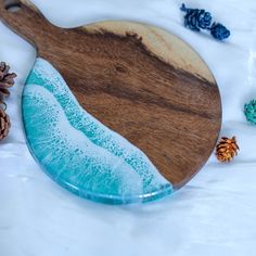 a wooden cutting board with blue and white paint on it next to pinecones