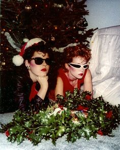 two women laying on the floor in front of a christmas tree wearing sunglasses and santa hats