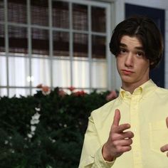 a young man in a yellow shirt is giving the thumbs up sign with both hands