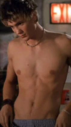 a shirtless young man is looking at his cell phone while standing in the kitchen