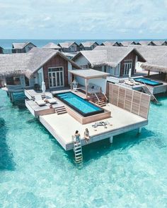 two people are standing on the dock in front of an over water villa with a swimming pool