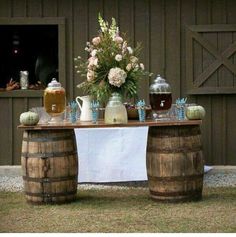 an outdoor table with vases and flowers on it in front of a barn door