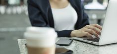 a woman sitting at a table with a laptop and cell phone in front of her