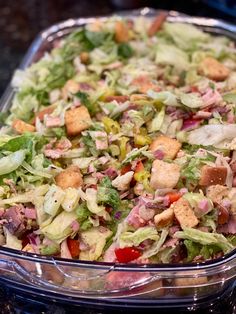 a salad in a glass dish on a counter top with croutons and lettuce