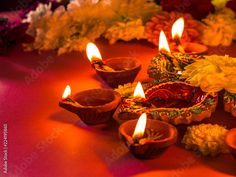 lit candles are placed on a table with flowers and petals around the candle holders in front of them