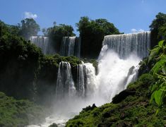 the waterfall is surrounded by greenery and blue skies in the background, with water cascading over it