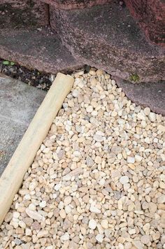 a wooden stick sitting on top of a pile of rocks next to a sidewalk and stone wall