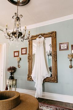 a wedding dress hanging on a hanger in front of a mirror and chandelier