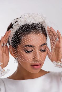 a woman wearing a veil and holding her hair in front of her face with both hands