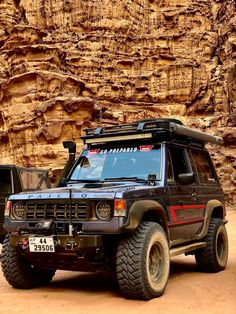 an suv parked in front of a large rock wall with a roof rack on it