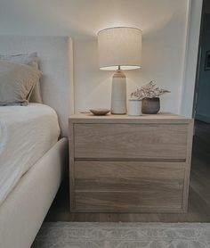 a white lamp sitting on top of a wooden dresser next to a bed in a bedroom