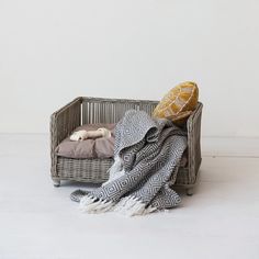 a wicker basket with a blanket and pillows on the floor in front of it