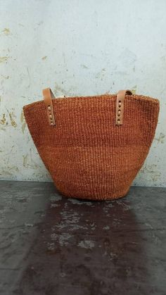 "Unique and stylish burned orange sisal kiondo bag with stitched leather straps. Ideal as a beach bag, shopping basket, market basket or storage basket. This unique tote bag is handmade by a group of ladies in a remote rural village in Machakos, Kenya. Do not clean with water. If the bag gets wet, please dry to avoid dampness.  Leather type used is bovine, from cattle. It's natural and in it's purest form. DIMENSIONS Bottom width: 10\"/25.5cm Top width: 14\"/35.56cm Depth: 10\"/25.5cm Straps: 15\"/38cm SHIPPING All orders ship via DHL Express (3-5) days delivery time." Eco-friendly Orange Rectangular Straw Bag, Brown Woven Leather Straw Bag With Double Handle, Brown Double Handle Woven Leather Straw Bag, Jute Bucket Bag For Market, Brown Jute Bucket Straw Bag, Brown Jute Bucket Bag With Braided Handles, Brown Rectangular Woven Leather Beach Bag, Natural Woven Leather Basket Bag, Natural Basket Shaped Woven Leather Bags