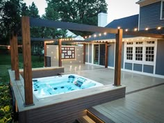 a hot tub sitting on top of a wooden deck next to a house with string lights