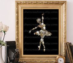 an ornate gold frame with a ballerina in the middle on a shelf next to some books and a clock