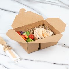 an open take out box filled with food next to a fork and knife on a marble surface