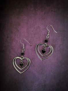 Introducing our stunning silver hollowed heart with black heart dangle earrings! These exquisite earrings are the perfect accessory to add a touch of elegance to any outfit. The intricate silver hollowed heart design is beautifully complemented by the dangling black heart, creating a unique and eye-catching look. Made with high-quality materials, these earrings are not only stylish but also lightweight and comfortable to wear all day long. Whether you're attending a special event or looking to elevate your everyday style, these silver hollowed heart with black heart dangle earrings are the perfect choice. Order now to add a little love and sophistication to your jewelry collection! Each product is one of a kind so there might be slight variations in colour, thickness, or shape. No two are Cute Black Earrings, Sterling Silver Earrings Dangle, Dark Feminine Earrings, Heart Jewelry Silver, Whimsigoth Earrings, Dark Earrings, Black Heart Earrings, Goth Earrings, Alternative Jewelry