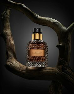 a bottle of perfume sitting on top of a wooden tree branch in front of a dark background