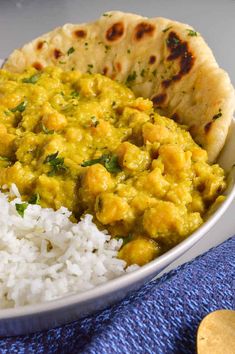 a bowl filled with rice and chicken curry next to pita bread on a blue towel