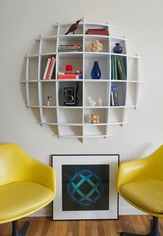 two yellow chairs sitting in front of a white book shelf filled with books and other items