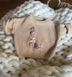 a knitted sweater with flowers on it laying on a pile of white cottons