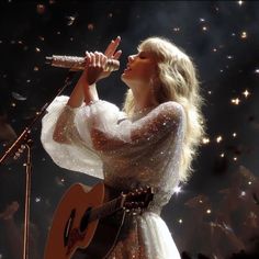 a woman in a white dress holding a guitar and singing into a microphone on stage