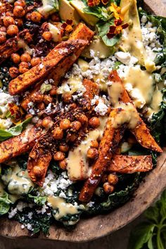 a salad with chickpeas, lettuce and cheese on top is served in a wooden bowl