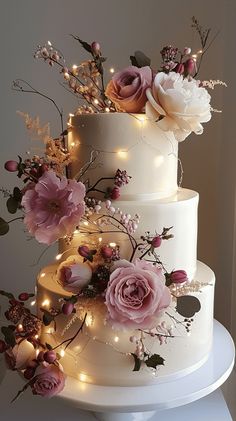 a three tiered wedding cake with pink flowers and lights on the top is decorated in white frosting